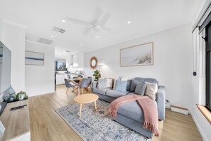 A modern living room with a grey sofa, a coffee table, and a dining area with chairs. - Two bedroom  in Australia, Henley Beach South (Henley Beach South)