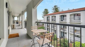 Un balcón con mesa y sillas, un felpudo y vista a un edificio con varios balcones.