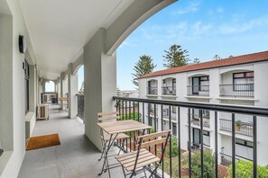 A balcony with a table and chairs, a doormat, and a view of a building with multiple balconies. - Two bedroom  in Australia, Henley Beach South (Henley Beach South)