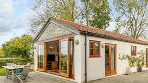 Un edificio de piedra con techo de tejas, puerta de cristal y un patio con mesa y sillas.