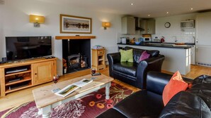 Una sala de estar con televisor, chimenea, sofá, mesa de centro y una cocina al fondo.