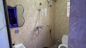 Uma casa de banho com chuveiro, sanita, lavatório e espelho.