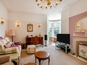 A living room with a sofa, ottoman, coffee table, fireplace, television, and a large window. - 2 Bed in Bexhill-on-sea (oc-95831) (Bexhill-on-Sea)