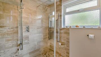 A bathroom with a glass shower enclosure, a window with a view, and a tiled floor.
