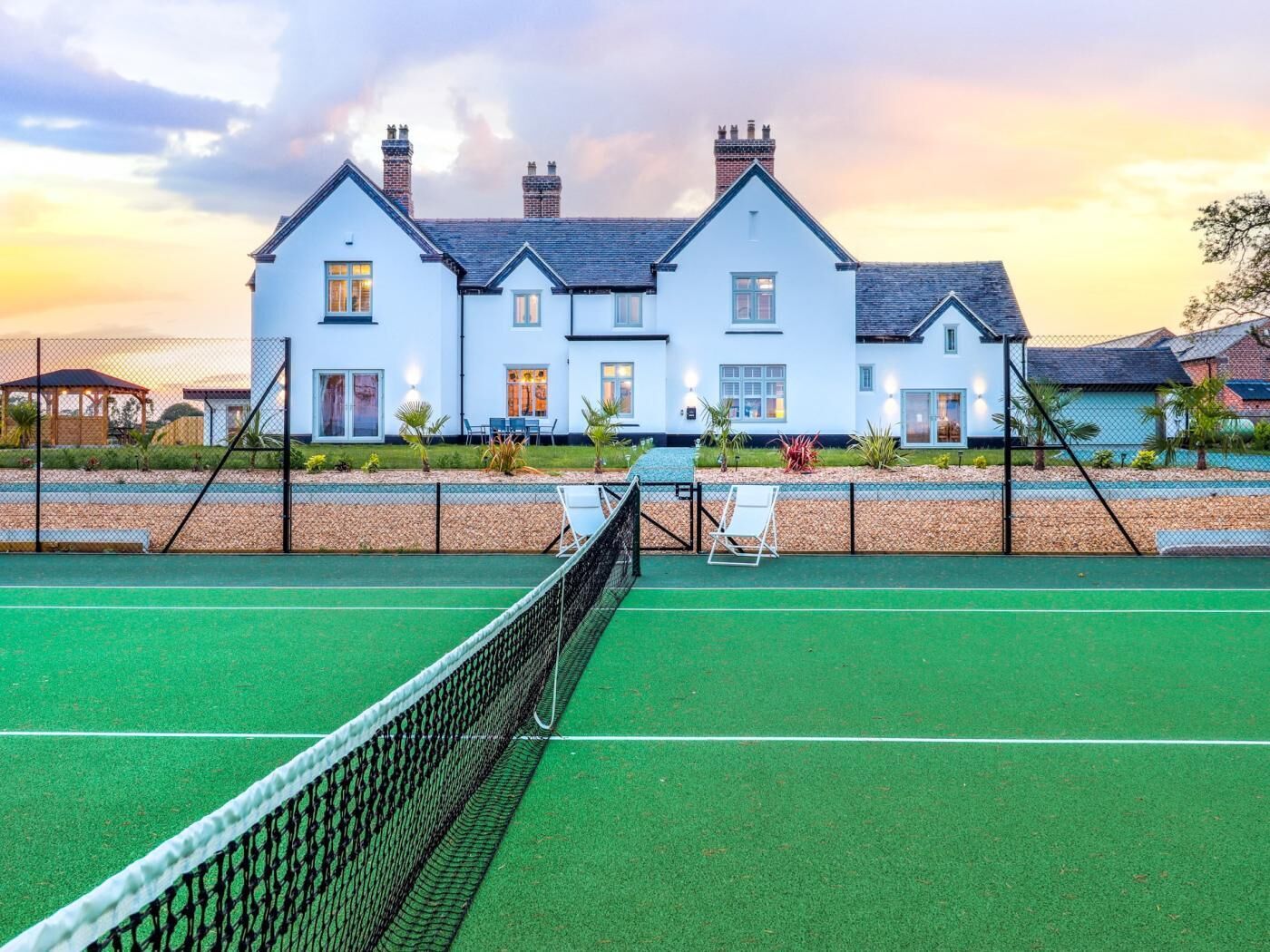 Un court de tennis avec un filet au premier plan et un grand bâtiment blanc avec de nombreuses cheminées en arrière-plan.