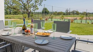 An outdoor dining area with a table set for two, surrounded by chairs, overlooking a tennis court and a grassy field. - 7 Bed in Whitchurch (oc-95835) (Wem Rural)