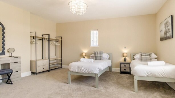 A bedroom with two beds, a vanity with a mirror, a wardrobe, and a chandelier. - 7 Bed in Whitchurch (oc-95835) (Wem Rural)