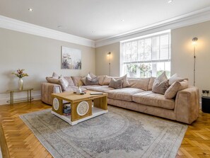 Un salon avec un canapé beige, une table basse en bois et un tapis à motifs.
