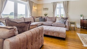 A spacious living room with a large L-shaped sectional sofa, a small side table, and a decorative wall piece. - 7 Bed in Whitchurch (oc-95835) (Wem Rural)
