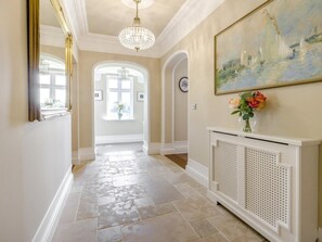 A hallway with a white console table, a painting, and a chandelier.