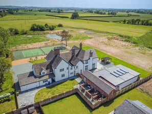 Une grande maison avec un court de tennis, une grange en briques et de vastes champs verdoyants.