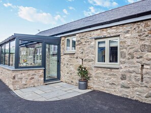 A stone building with a glass conservatory, a potted plant, and a paved entrance. - 2 Bed in Denbigh (oc-95843) (Llannefydd)