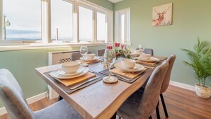A dining area with a wooden table set for four, large windows, and a chandelier. - 2 Bed in Bonnybridge (oc-95833) (Bonnybridge)