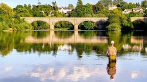 Une rivière paisible, avec un pont de pierre et des maisons en arrière-plan.