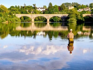 Ein ruhiger Fluss mit einer Steinbrücke und Häusern im Hintergrund.