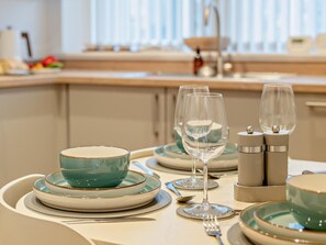 Una mesa de comedor lista con platos, tazones, vasos y cubiertos, con una cocina al fondo.