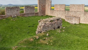 Une structure en pierre d’importance historique, avec des ruines, un terrain herbeux et des champs situés au loin.