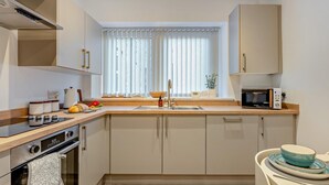 Une cuisine moderne équipée d’un four encastré, d’un four à micro-ondes et d’une fenêtre avec des stores.