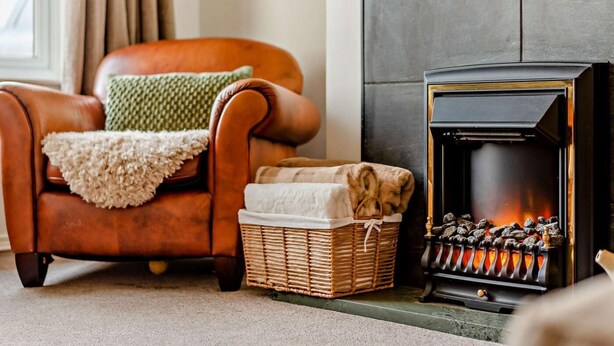 A cozy living room with a leather armchair, a fireplace, and a wicker basket. - 3 Bed in Keswick (oc-95858) (Keswick)