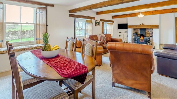 Een eethoek met een houten tafel, stoelen, een schaal fruit en een rode tafelkleed.