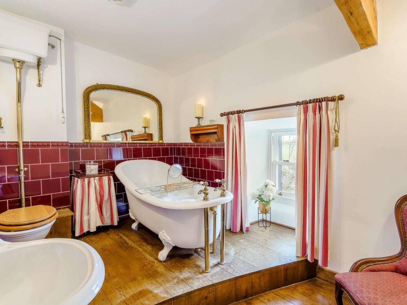 Une salle de bain avec une baignoire sur pieds, un lavabo, un miroir et une fenêtre avec des rideaux.