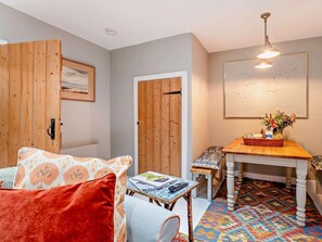 A cozy room with a wooden door, a bench, a table with a basket, and a colorful patterned rug.