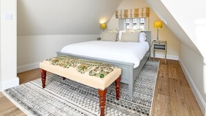 Ein Schlafzimmer mit Bett, Sitzbank, Nachttischen, Lampen und einem Fenster mit Vorhängen.