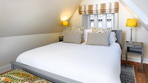 Ein Schlafzimmer mit einem großen Bett, zwei Nachttischen mit Lampen, einem Fenster mit Jalousien und einem gemusterten Teppich.