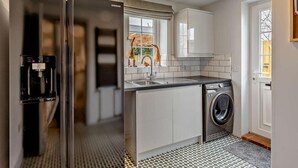 Eine moderne Küche mit einem Edelstahl-Kühlschrank, einem integrierten Wasserspender, einer Waschmaschine und einem Fenster mit Blick ins Freie.