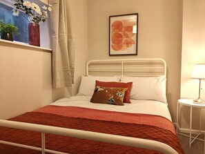 Una cama con estructura metálica, ropa de cama blanca y un plaid rojo estampado.