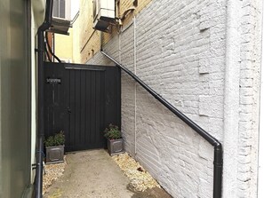 Un estrecho callejón con una verja negra, paredes de ladrillo blanco y dos macetas.