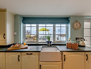 A kitchen with a window view, a clock, and a kettle on the counter. - 2 Bed in Ravenglass (oc-95884) (Muncaster)