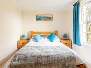 A bedroom with a bed, two bedside tables, a nightstand, a window with curtains, and a wall-mounted picture. - 5 Bed in Bude (oc-60291) (Morwenstow)