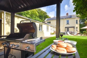 An outdoor grill area with a table set for a meal, including bread and a glass of red wine. - 5 Bed in Bude (oc-60291) (Morwenstow)