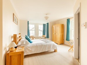 Ein Schlafzimmer mit Bett, Nachttisch, Lampe, Kleiderschrank und zwei mit Vorhängen versehenen Fenstern.