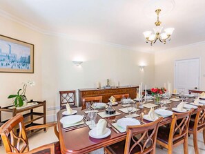 A dining room with a long table set for a meal, a chandelier, and a painting on the wall. - 5 Bed in Bude (oc-60291) (Morwenstow)