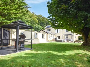 Ein überdachter Grillbereich mit Grill, einer Rasenfläche und einem Haus im Hintergrund.