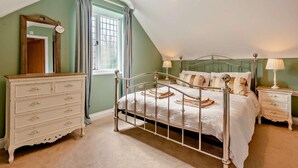Een slaapkamer met een metalen bedframe, een dressoir, een nachtkastje, een lamp en een raam met gordijnen.