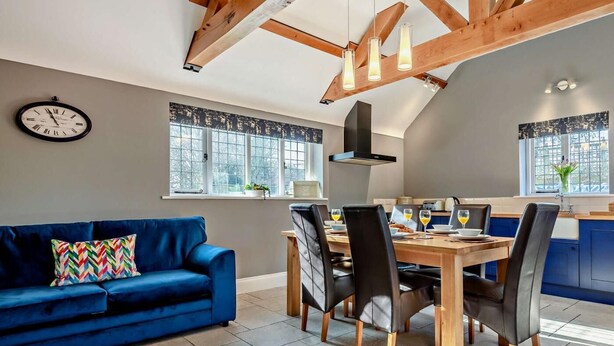 Een moderne keuken met houten balken, een eettafel met stoelen, een blauwe bank en een klok aan de muur.