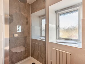 Ein Badezimmer mit Duschkabine aus Glas, einem Fenster mit Milchglas und einem weißen Heizkörper.