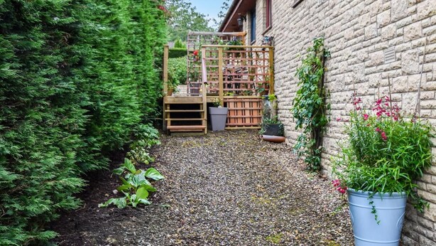 Een tuin met een houten trelislat, een grindpad en een bakstenen gebouw.