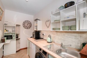 Eine kleine Küche mit Mikrowelle, Toaster, Wasserkocher und Spüle. Regale mit Geschirr und eine Uhr an der Wand.