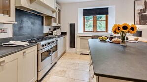 A modern kitchen with a gas stove, oven, and a window with a view of greenery. - 4 Bed in Ilfracombe (oc-95899) (Berrynarbor)