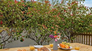 A wooden picnic table with plates of food, glasses of orange juice, and a vase of flowers. - 4 Bed in Ilfracombe (oc-95899) (Berrynarbor)