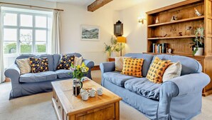 Ein Wohnzimmer mit zwei Sofas, einem Couchtisch, einem Bücherregal aus Holz und einem Fenster mit Vorhängen.