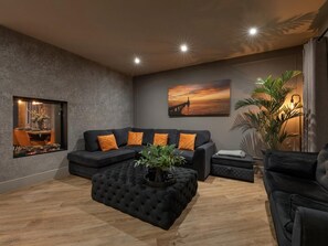 A modern living room with a sectional sofa, a tufted ottoman, a dining area with a view, and a large landscape painting on the wall. - 4 Bed in Morpeth (oc-95889) (Amble)