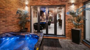 A spa area with a hot tub, potted plants, and a dining area visible through glass doors. - 4 Bed in Morpeth (oc-95889) (Amble)
