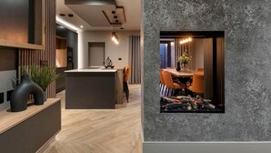 A modern kitchen with a central island, a dining area with a fireplace, and a textured wall. - 4 Bed in Morpeth (oc-95889) (Amble)