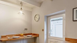 A kitchen with a wooden countertop, two stools, a hanging light fixture, a wall clock, and a window. - 2 Bed in Fowey (oc-91015) (Polruan)