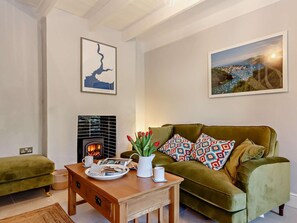 Ein Wohnzimmer mit einem grünen Sofa, einem Holztisch mit Frühstücksgebäck, einem Kamin und zwei gerahmten Bildern an der Wand.